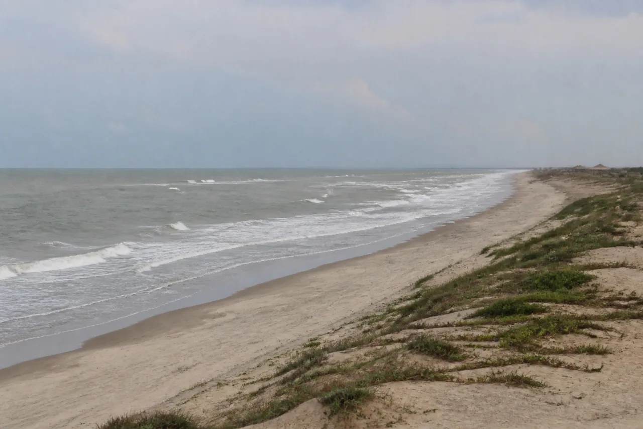 Playa larga de arena clara y oleaje suave del Golfo, con dunas bajas.