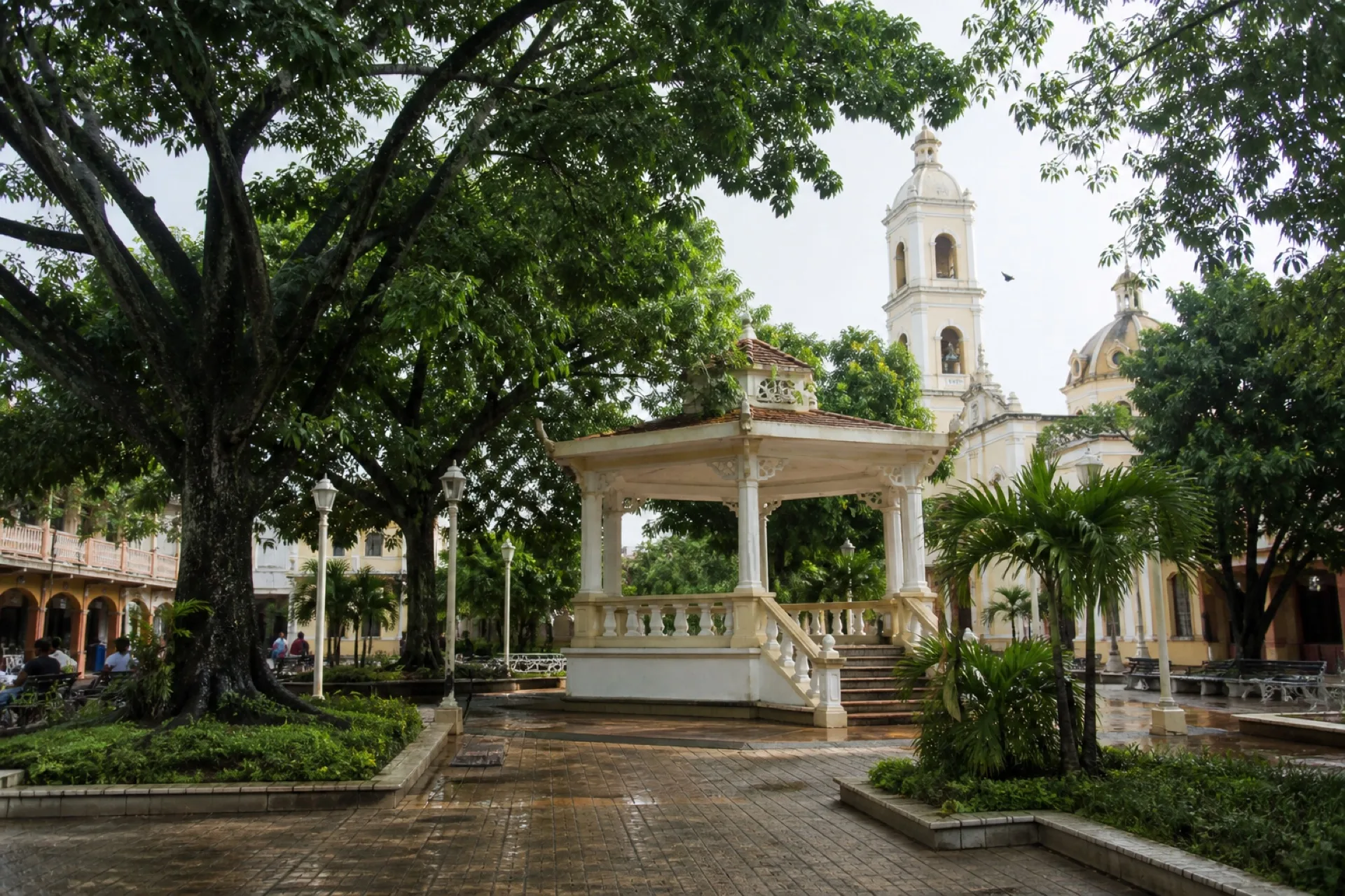 Parque central de Acayucan con kiosco y torres de parroquia al fondo.