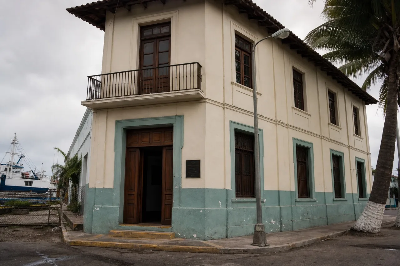 Fachada de un museo municipal de dos pisos en un puerto del Golfo, con muelle al fondo.